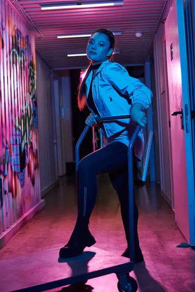 A beautiful woman showcases her bold style while standing with a cart in an artistic corridor. — Stock Photo