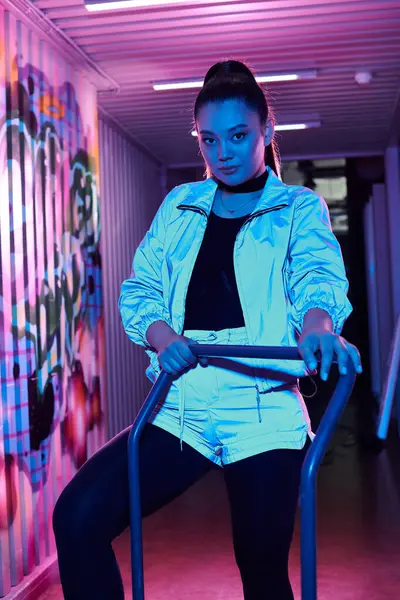 A beautiful woman exudes style and confidence in a brightly lit corridor with stunning graffiti. — Stock Photo