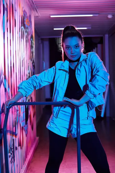 A stylish woman poses confidently amid vibrant street art at dusk. — Stock Photo