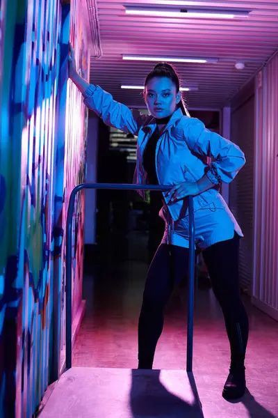 Una mujer impresionante posa junto a un vibrante mural en una moderna escena urbana nocturna. - foto de stock