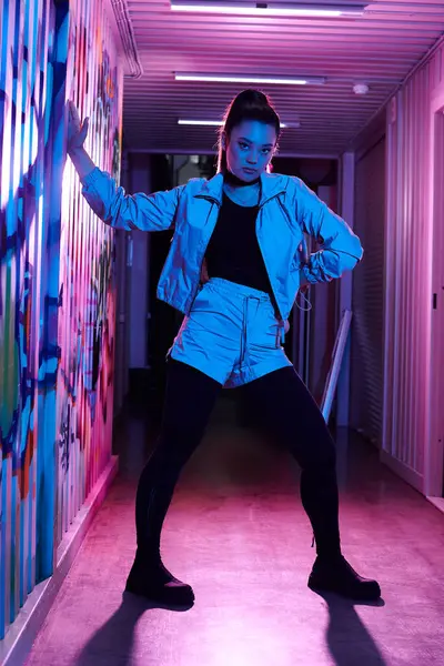 Eine modische Frau posiert kraftvoll in einer bunten Gasse, die mit Street Art geschmückt ist. — Stockfoto