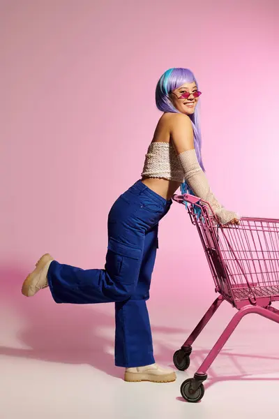 A beautiful woman in trendy attire strikes a fun pose with a shopping cart in a vibrant setting. — Stock Photo