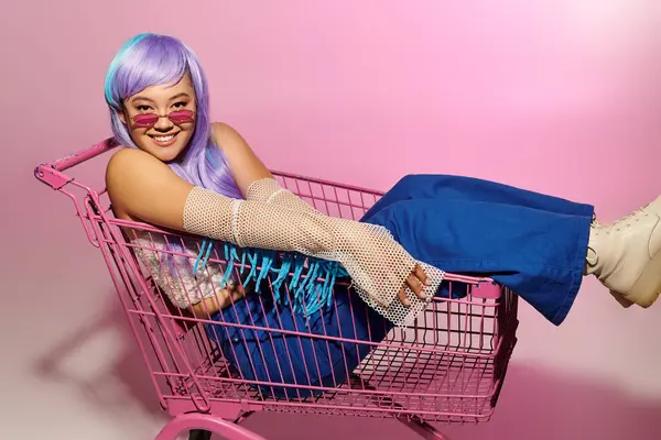 A stylish woman relaxes in a shopping cart, flaunting her unique style in a colorful setting. — Stock Photo