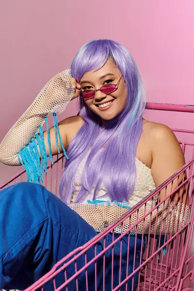 Mujer de moda hacia adelante con gafas de sol elegantes de pelo lavanda mientras se relaja en un carrito colorido. - foto de stock