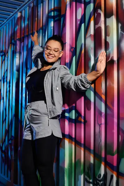 In a vibrant city, a stylish woman poses joyfully next to colorful graffiti. — Stock Photo