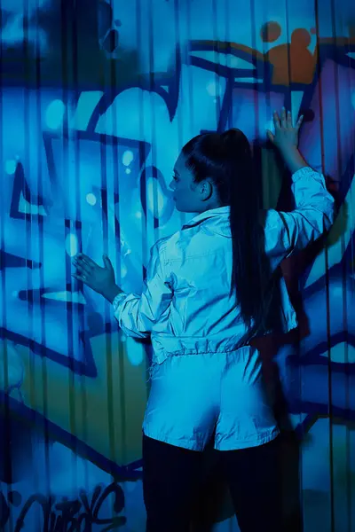 Una mujer con estilo interactúa con un graffiti vibrante en un entorno urbano. - foto de stock