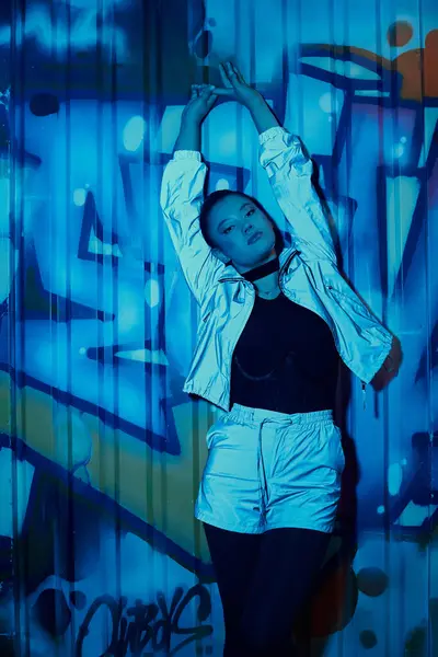 Femme à la mode pose gracieusement sur un fond de graffiti vif sous un éclairage doux. — Photo de stock