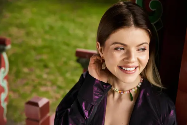 Young woman smiles in pavilion, bright outfit necklace. — Stock Photo