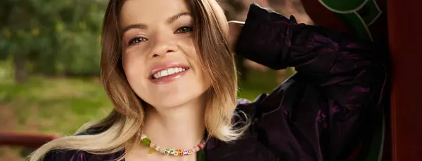 Smiling woman in park, spring necklace, stylish jacket. — Stock Photo