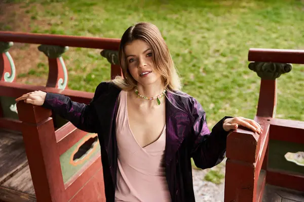 A pretty young woman stands by a painted wooden fence in a park. — Stock Photo