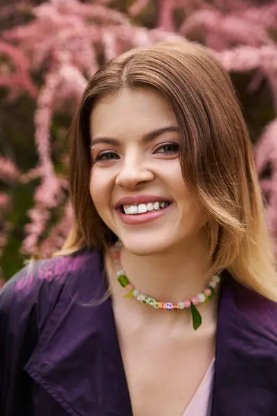 Smiling young woman with necklace by pink blossoms. — Stock Photo