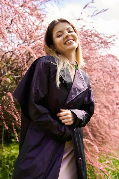 Smiling girl in dark coat, pink spring flowers. — Stock Photo