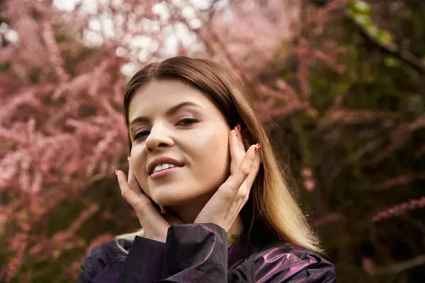 Beautiful woman smiles, hands on her face. Surrounded by pink blossoms. — Stock Photo