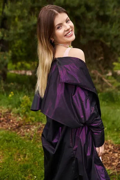 Smiling woman in purple jacket looks back in meadow. — стоковое фото
