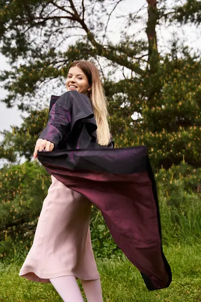 Smiling, she twirls her coat, happy in nature. — стоковое фото