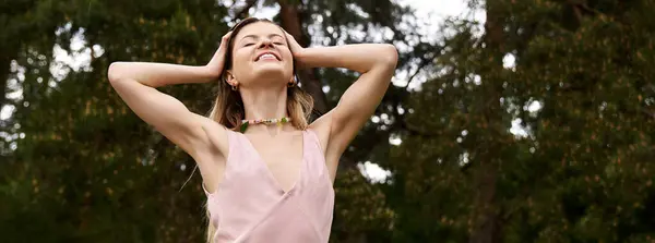 A young woman with arms raised above her head smiles contentedly under the trees on a bright day. — Stock Photo