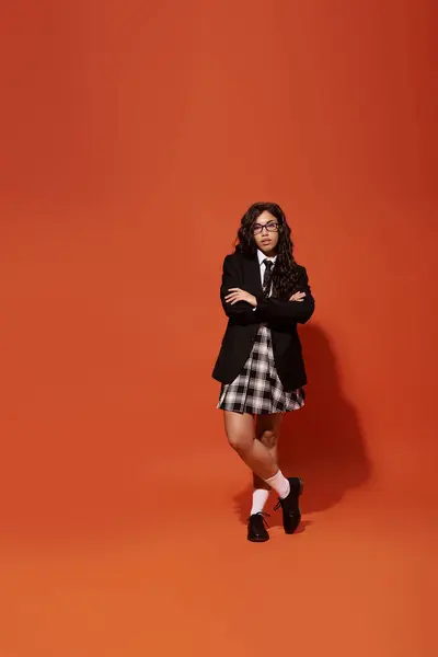 Donna sicura di sé si alza con le braccia incrociate, mostrando il suo stile studente chic ed energia vibrante. — Foto stock