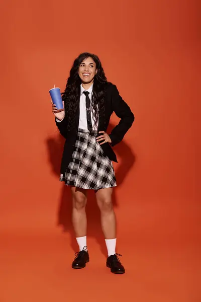 Brillantemente vestita giovane donna posa con un drink su un audace sfondo arancione. — Foto stock