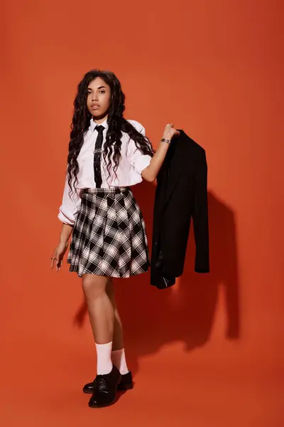 Une jeune étudiante confiante tient sa veste sur un fond orange vif. — Photo de stock