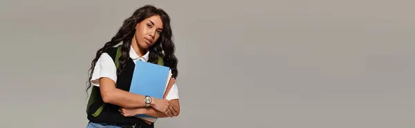 A young woman with a confident vibe embraces her books, exuding student elegance in a neutral space. — Stock Photo