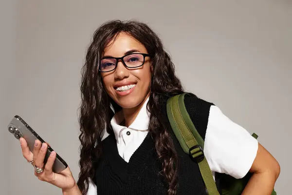 A beautiful young woman smiles brightly while holding her smartphone, embodying student aesthetics. — Stock Photo