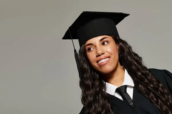 Hermosa estudiante lleva gorra de graduación y vestido, sonriendo con orgullo y emoción en sus ojos. - foto de stock