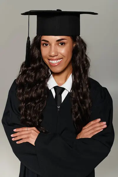 Una hermosa joven vestida de graduación posa orgullosamente con los brazos cruzados, sonriendo brillantemente. - foto de stock