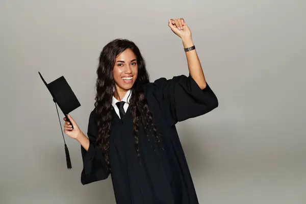 Young woman in a graduation gown joyfully celebrating her academic achievement with a hat — Stock Photo