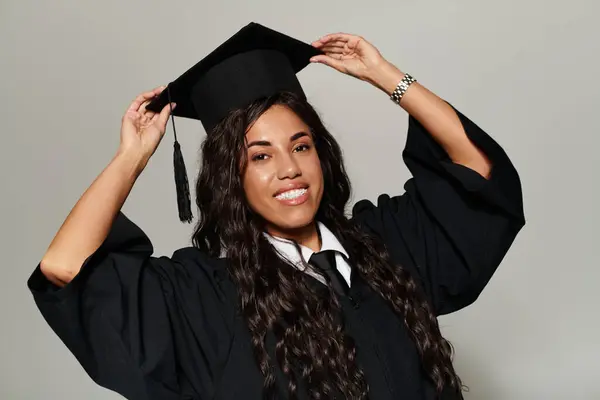 Una joven mujer ajusta alegremente su gorra de graduación con un vestido llamativo. - foto de stock