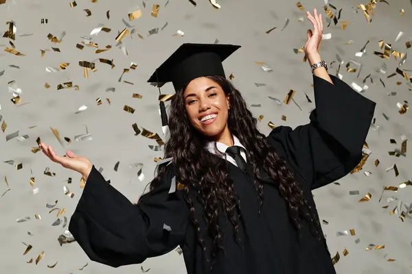 Una joven vestida de graduación sonríe alegremente mientras cae confeti a su alrededor.. - foto de stock