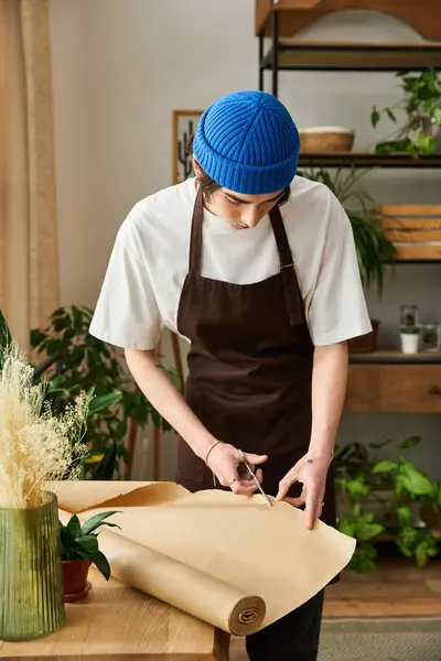 A young man in a blue beanie carefully transplants plants in a bright studio. — Stock Photo