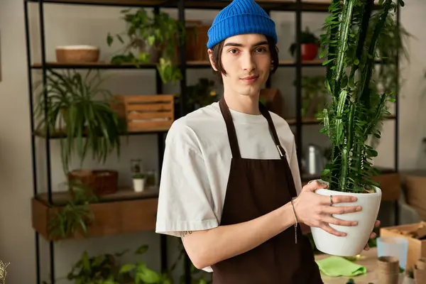 Young man wearing a blue beanie carefully arranges thriving plants in a cozy studio environment. — Stock Photo