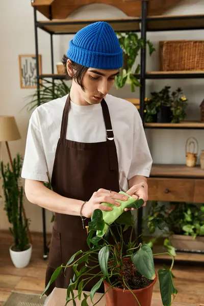 A young man in a brown apron tenderly transplants a green plant while surrounded by greenery. — Stock Photo
