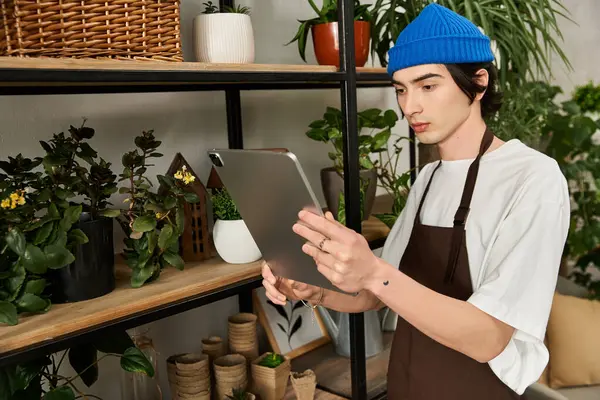 Young man actively tending to plants while consulting an electronic device in a vibrant studio. — Stock Photo