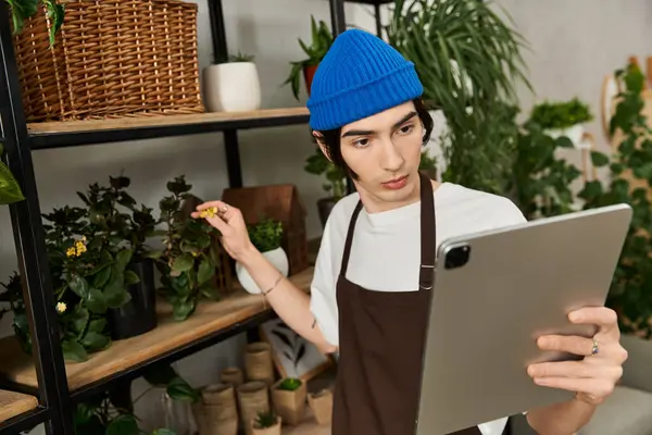 Joven en un elegante estudio con cuidado tiende a sus plantas utilizando una tableta para la orientación. - foto de stock