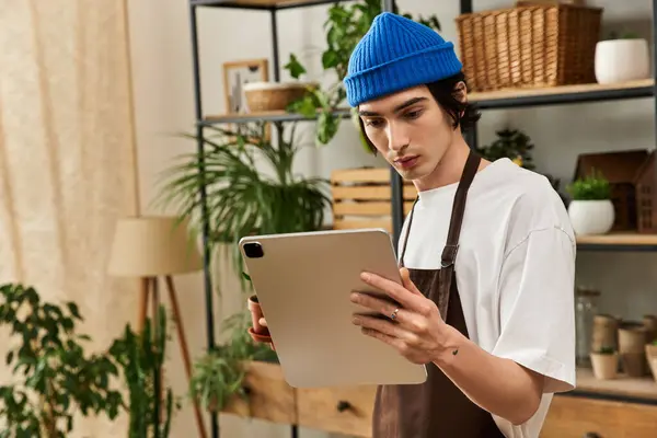 Young man in a blue beanie explores plant care techniques while nurturing greenery indoors. — Stock Photo
