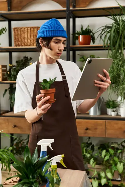 Guapo joven trasplante de plantas y tableta de consultoría en un vibrante espacio de jardín interior. - foto de stock