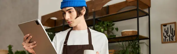 Young man in an apron uses a tablet to check plant care in a greenery filled studio. — Stock Photo