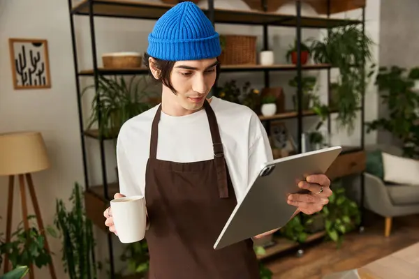 Handsome young man wearing an apron and beanie is transplanting plants in a stylish studio setting. — Stock Photo