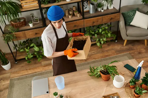 Handsome young man focuses on transplanting plants while surrounded by a lush indoor garden. — Stock Photo
