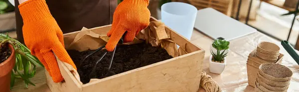 Young man with orange gloves nurturing plants in a vibrant studio, surrounded by greenery. — Stock Photo