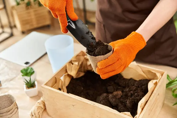 Young man with gloves carefully fills a pot with soil while transplanting plants indoors. — Stock Photo