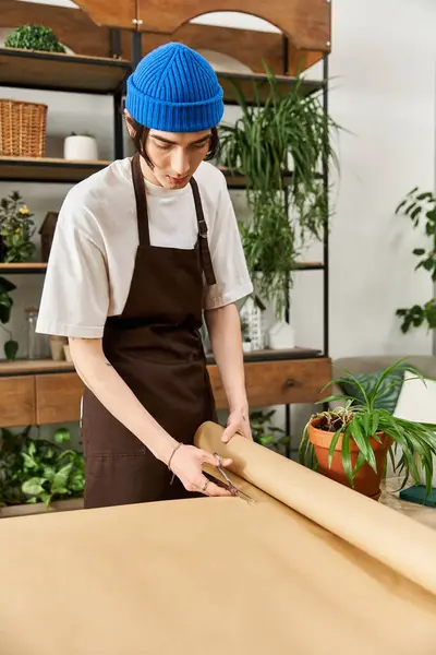 Young man in an apron is skillfully wrapping plants in a vibrant studio surrounded by nature. — Stock Photo