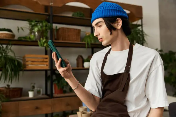 A young man in a brown apron is transplanting plants while focused on his phone. — Stock Photo
