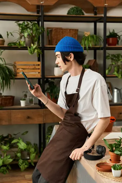 Handsome young man carefully checking his phone while surrounded by thriving houseplants. — Stock Photo