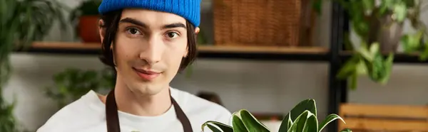 Handsome young man carefully holding fresh green plant in a sunny studio filled with life. — Stock Photo