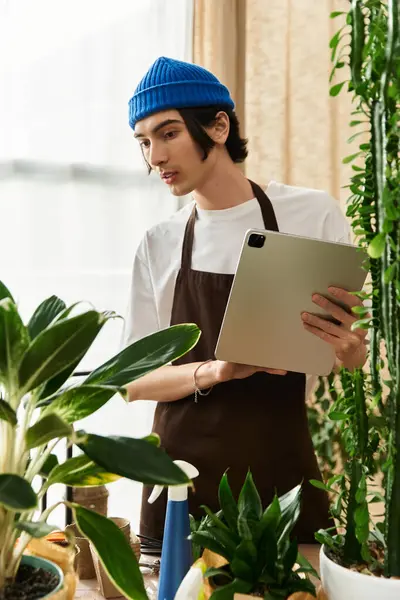 Joven en el estudio trasplanta cuidadosamente las plantas mientras usa una tableta para guiar su trabajo. - foto de stock