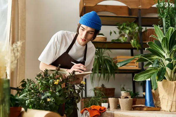 Young man engaged in transplanting various plants in vibrant indoor studio environment, take notes. — Stock Photo