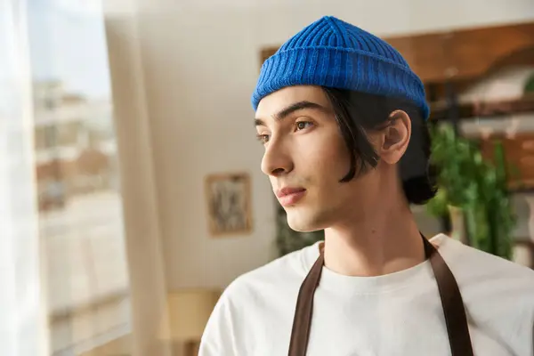A handsome young man among lush plants in a sunlit studio, focused and attentive. — Stock Photo