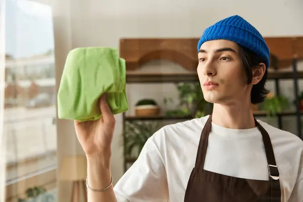 Young man washing glass in a studio filled with natural light and greenery. — Stock Photo